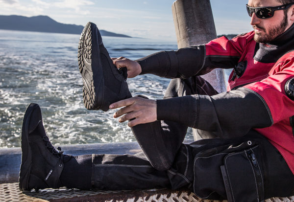 Man wearing a Bear Drysuit and sunglasses putting on Bear drysuit rock boots