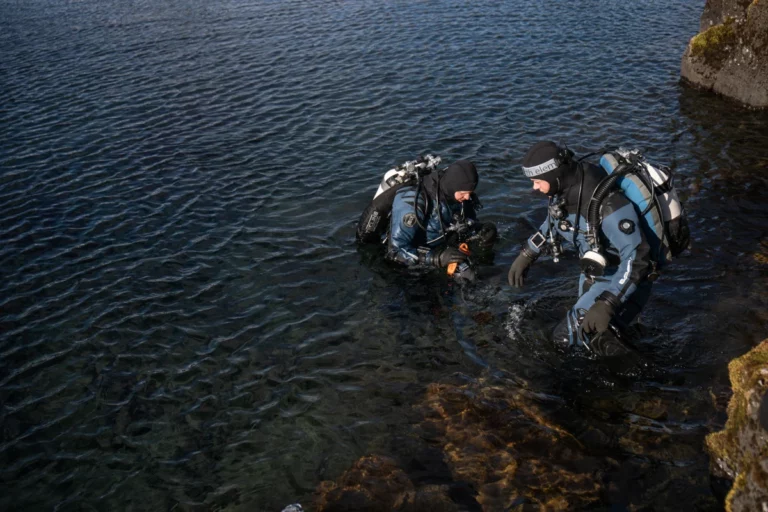 two scuba divers in fourth element trilaminate drysuits entering the water from rocks