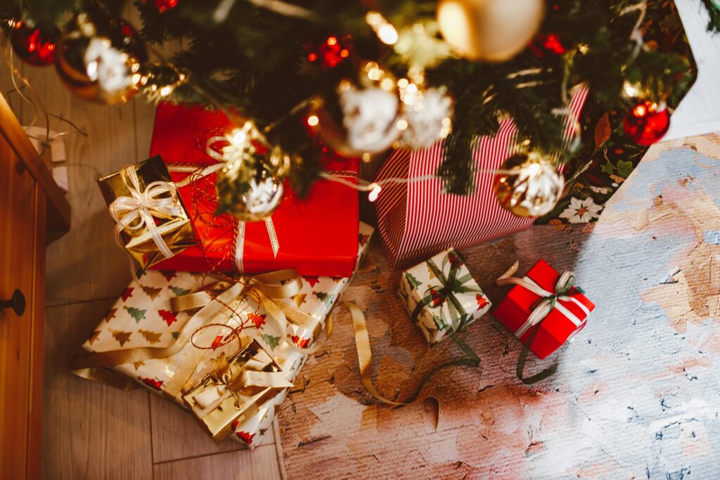 Beautifully wrapped gifts under a decorated Christmas tree with ornaments and lights.